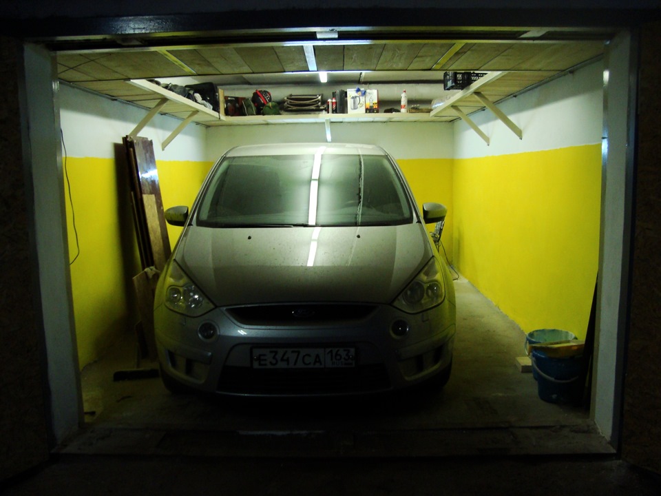 Дизайн гаража с желто-белыми крашеными стенами и полками под потолком по периметру