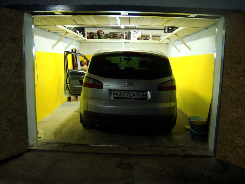 Дизайн гаража с желто-белыми крашеными стенами и полками под потолком по периметру
